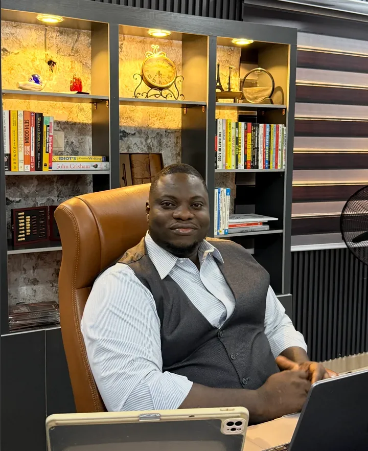 Fredrick Eghosa at his desk in his office, in front of a lit bookshelf